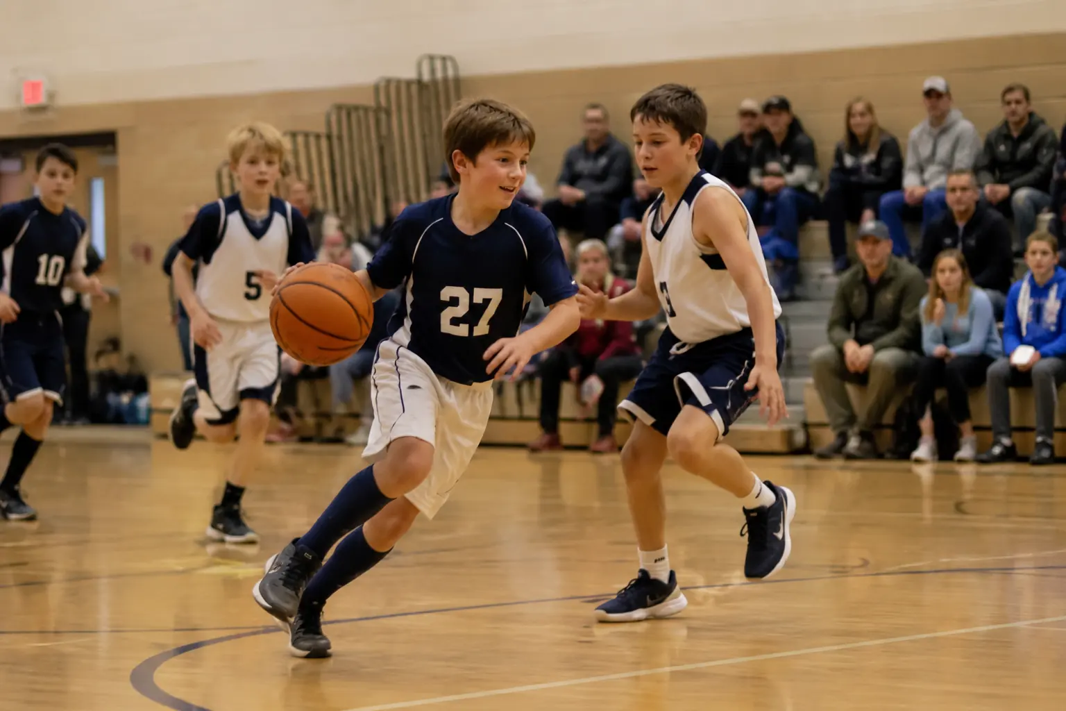 Winter basketball, the steal. Illustrative photo of a youth basketball player in a navy number 27 jersey, about ten years old, driving up the court in a packed school gym.