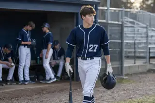 Illustrative photo of a high school baseball player, about fifteen years old, walking with a bat in team gear.