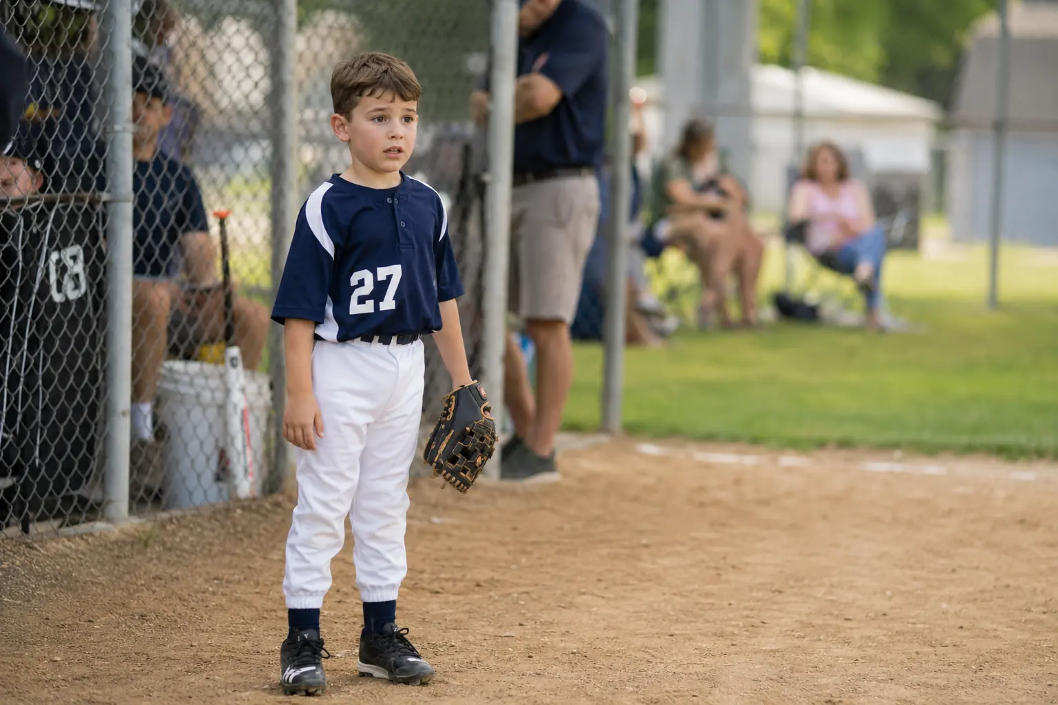 First practice. Illustrative photo of a young rec-league baseball player, about seven years old, standing on a dirt infield in a navy uniform.